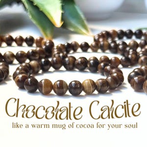 May include: Close-up of several strands of chocolate calcite bead bracelets. The beads are a mix of brown and tan, with a polished, smooth surface. The text "Chocolate Calcite" is displayed in a decorative font, with the phrase "like a warm mug of cocoa for your soul" below.