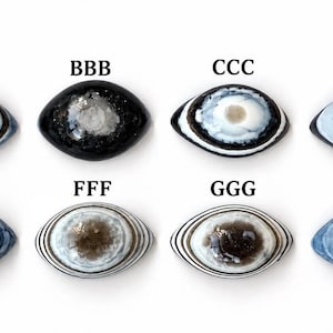 May include: Eight oval-shaped cabochons arranged in two rows, labelled AAA through HHH. Each piece features distinct patterns including concentric rings, dark centres, and blue, white, and black colour variations. The stones have a smooth, polished surface with varied textures and colour gradients throughout the collection.