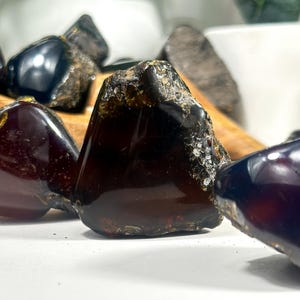 Puede incluir: Una colecci&oacute;n de piedras de &aacute;mbar oscuro de diferentes formas y tama&ntilde;os. Las piedras tienen un acabado brillante y algunas tienen un ligero brillo.