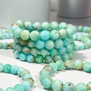 May include: Several bracelets made of round, light blue and green beads. The beads have a marbled appearance with variations in color. The bracelets are stacked and scattered, showcasing the jewelry's design and color variations.