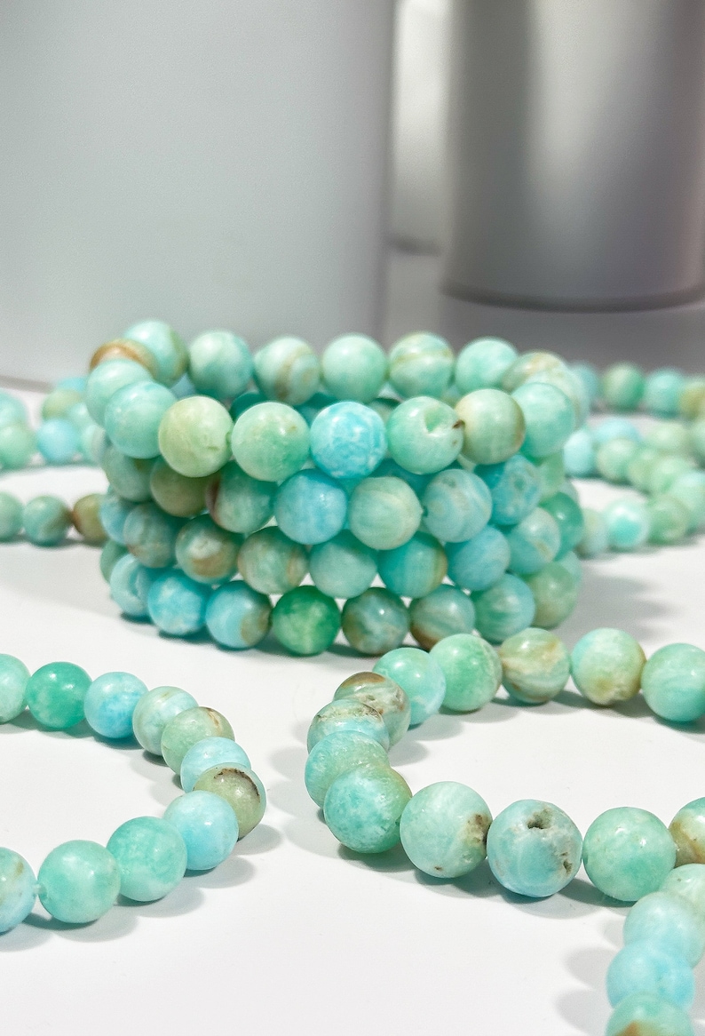 May include: Several bracelets made of round, light blue and green beads. The beads have a marbled appearance with variations in color. The bracelets are stacked and scattered, showcasing the jewelry's design and color variations.