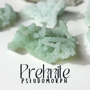 May include: A cluster of green prehnite crystals, a type of mineral, in a pseudomorph formation. The crystals are clustered together in a rough, irregular shape.