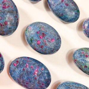 May include: A collection of smooth, polished oval stones featuring a deep blue base colour with scattered, vibrant magenta and pink inclusions throughout. Each stone displays a unique, mottled pattern of blue, purple, and pink mineral deposits.