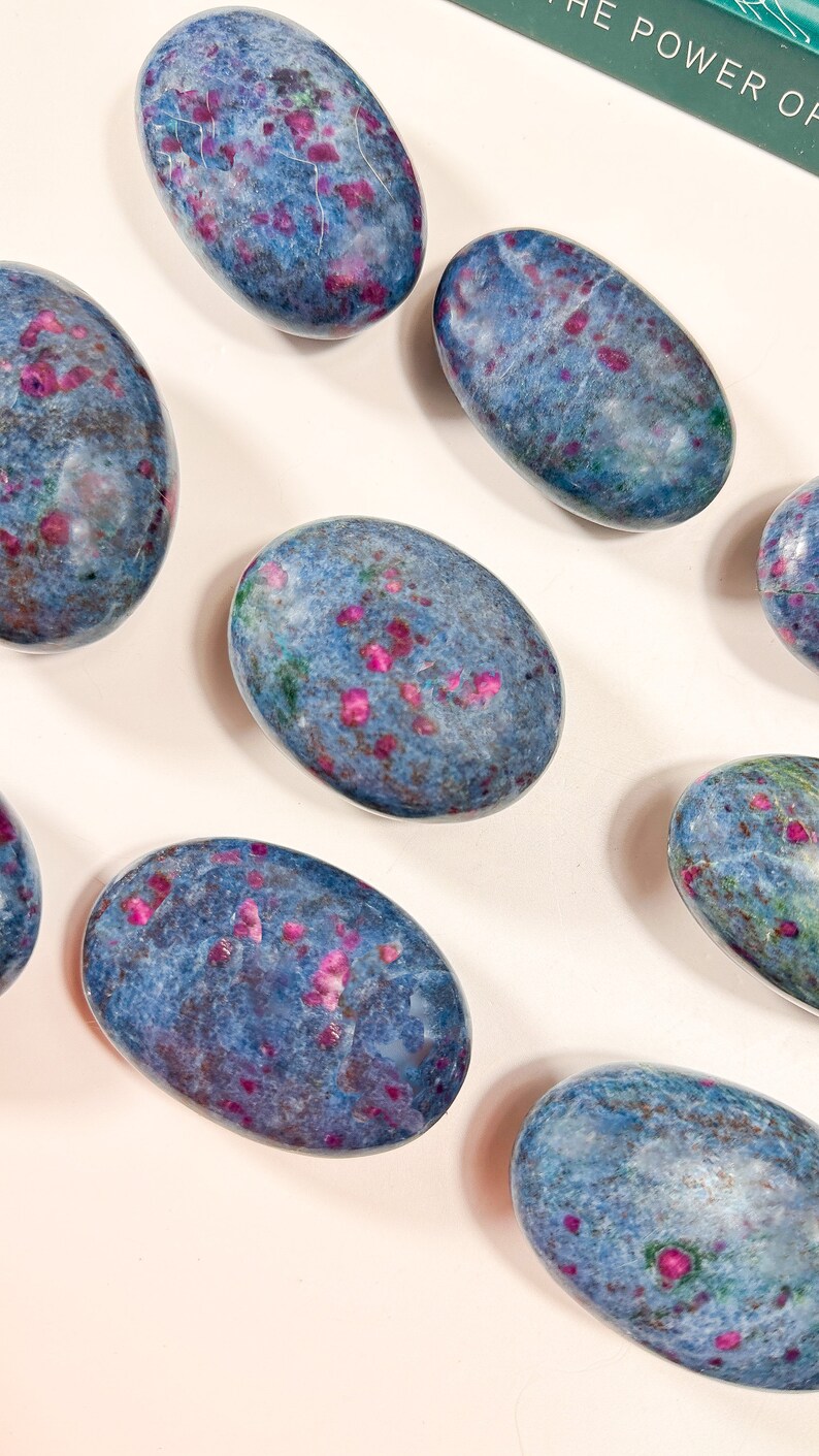 May include: A collection of smooth, polished oval stones featuring a deep blue base colour with scattered, vibrant magenta and pink inclusions throughout. Each stone displays a unique, mottled pattern of blue, purple, and pink mineral deposits.