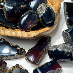 Puede incluir: Una colecci&oacute;n de piedras de &aacute;mbar oscuro con un tono rojizo. Las piedras son de varias formas y tama&ntilde;os y tienen un acabado brillante.