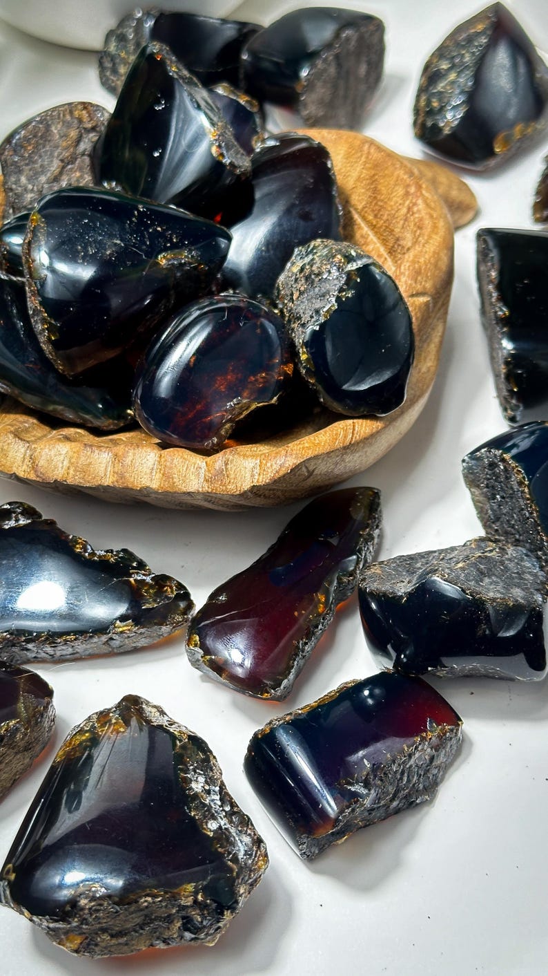 Puede incluir: Una colecci&oacute;n de piedras de &aacute;mbar oscuro con un tono rojizo. Las piedras son de varias formas y tama&ntilde;os y tienen un acabado brillante.