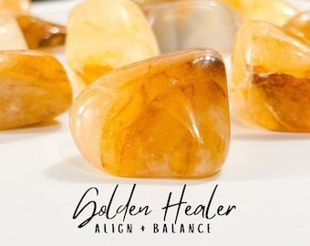 May include: A collection of golden healer tumbled stones. The stones are a light orange color with a translucent quality. The stones are smooth and polished. The text "Golden Healer ALIGN + BALANCE" is written below the stones.