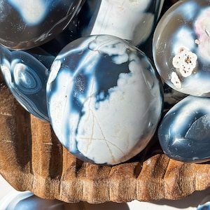 May include: A collection of polished agate stones with a variety of blue and white patterns. The stones are smooth and have a natural, organic look.