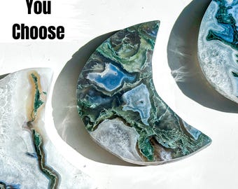 May include: Three crescent moon shaped agate slices with green, blue, and white patterns. The agate slices are polished and have a smooth surface.