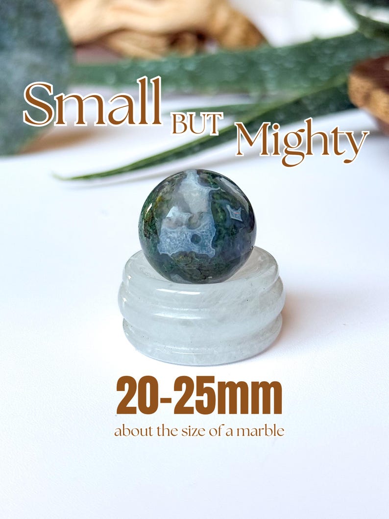 May include: A small, round, moss agate gemstone, approximately 0.79 to 0.98 inches in diameter, rests on a clear, circular stand. The image includes the text "Small BUT Mighty" and "20-25mm about the size of a marble."