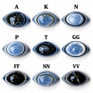 May include: Nine oval-shaped cabochons arranged in a grid, each featuring blue and black concentric patterns. The items are labelled with letters A, K, N, P, T, GG, FF, NN, and VV. Each piece displays a smooth, polished surface with unique variations in colour intensity and internal veining, resembling eye-like designs.