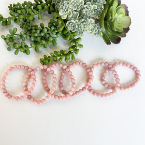May include: Five pink gemstone bracelets made of round beads. The bracelets are stacked on top of each other.