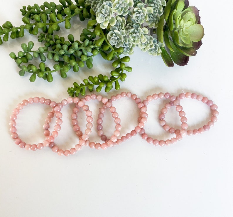 May include: Five pink gemstone bracelets made of round beads. The bracelets are stacked on top of each other.