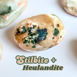 Op de afbeelding: Close-up van verschillende gepolijste stenen, elk met een unieke mix van kleuren. De stenen hebben een mix van beige, perzik, groen en blauw. De tekst "Stilbite + Heulandite" wordt weergegeven.