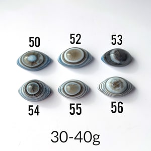 May include: Six oval-shaped banded agate stones arranged in two rows, labelled with numbers 50, 52, 53, 54, 55, and 56. Each stone features concentric circular patterns in shades of blue, grey, and white. The text 30-40g is printed at the bottom.