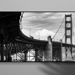 Può includere: Fotografia in bianco e nero del Golden Gate Bridge a San Francisco. L'immagine cattura le torri, i cavi e la carreggiata del ponte, con un cielo nuvoloso sullo sfondo. Un segnale di limite di velocità indica 45.