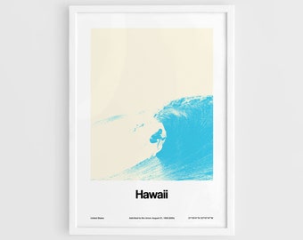 May include: A framed art print featuring a surfer riding a large blue wave. The word "Hawaii" is printed in black at the bottom, with additional text below. The background is a light cream color.