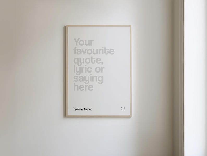 May include: A framed print with a light wood-coloured frame hangs on a white wall. The print features the text "Your favourite quote, lyric or saying here" in a light grey font. Below the text is "Optional Author".