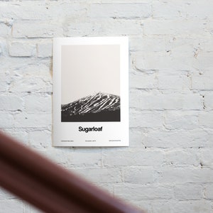 May include: A black and white photograph of Sugarloaf Mountain in Maine. The mountain is covered in snow and has ski trails visible. The text "Sugarloaf" is printed below the image.