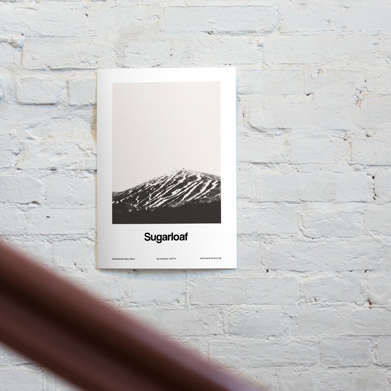 May include: A black and white photograph of Sugarloaf Mountain in Maine. The mountain is covered in snow and has ski trails visible. The text "Sugarloaf" is printed below the image.