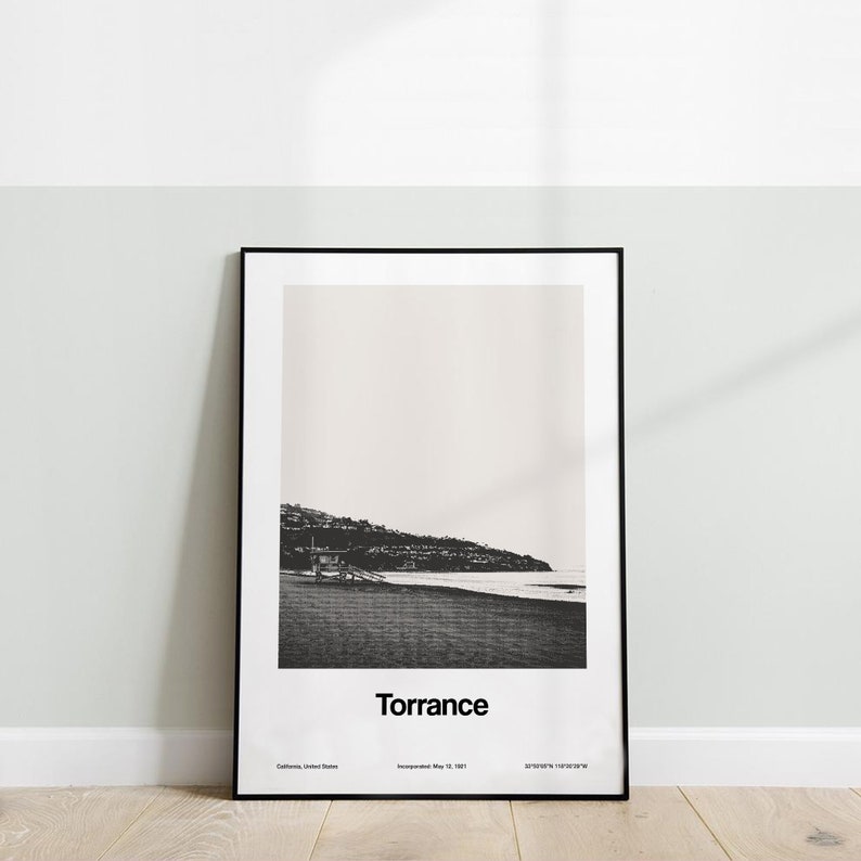 Pode incluir: Fotografia a preto e branco de uma cena de praia com uma torre de salva-vidas &agrave; dist&acirc;ncia. O texto "Torrance" est&aacute; impresso abaixo da imagem, juntamente com a localiza&ccedil;&atilde;o da cidade, a data de incorpora&ccedil;&atilde;o e as coordenadas.