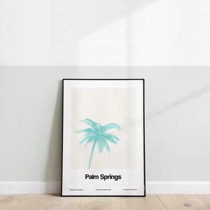 Pu&ograve; includere: Un poster incorniciato in nero con uno sfondo beige chiaro che presenta una palma turchese e il testo "Palm Springs" in nero. Il poster include anche il testo "California, United States" e "Incorporated April 26, 1938".