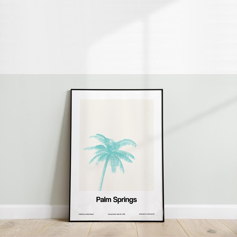 Pu&ograve; includere: Un poster incorniciato in nero con uno sfondo beige chiaro che presenta una palma turchese e il testo "Palm Springs" in nero. Il poster include anche il testo "California, United States" e "Incorporated April 26, 1938".