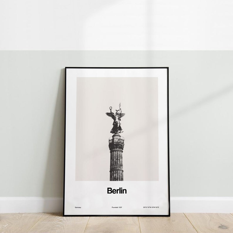 May include: Black and white photo of a statue of an angel on top of a column in Berlin, Germany. The photo is framed in a black frame. The text "Berlin" is printed below the image.