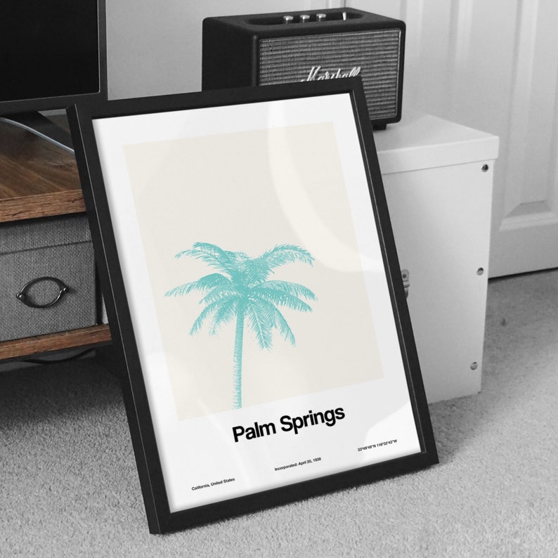 Pu&ograve; includere: Un poster incorniciato in nero con sfondo bianco e un'illustrazione di palma turchese. Il testo "Palm Springs" &egrave; stampato in nero nella parte inferiore del poster. Il testo "California, United States" e "Incorporated April 26, 1938" &egrave; stampato in nero pi&ugrave; piccolo sotto il testo principale.