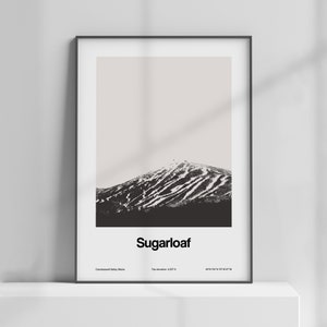 May include: A black and white photograph of Sugarloaf Mountain in Carrabassett Valley, Maine. The mountain is covered in snow and has ski runs visible. The text "Sugarloaf" is printed below the image, along with the mountain's top elevation and coordinates.