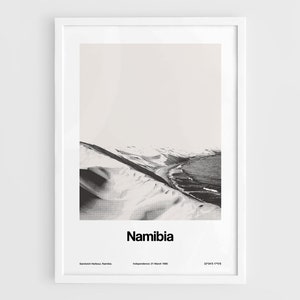 Op de afbeelding: Een zwart-witfoto van een woestijnlandschap in Namibi&euml;. De foto toont een zandstrand met een kustlijn en een bergketen op de achtergrond. De tekst "Namibi&euml;" is onder de afbeelding gedrukt.