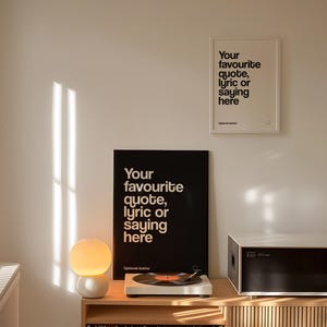 May include: An interior shot showing two framed prints with the text "Your favourite quote, lyric or saying here." A record player, a spherical lamp, and a stereo are on a wooden cabinet. The room is illuminated by sunlight.