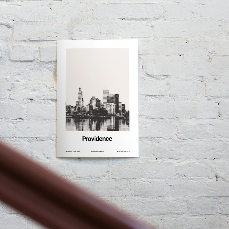Op de afbeelding: Zwart-witfoto van de skyline van Providence, Rhode Island. De skyline van de stad wordt weerspiegeld in het water. De tekst "Providence" is onder de afbeelding gedrukt.