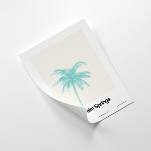 Pu&ograve; includere: Un poster minimalista con una silhouette di palma turchese su uno sfondo crema. Il testo "Palm Springs" &egrave; in basso sul poster, con la data "December 10, 1958" sotto.