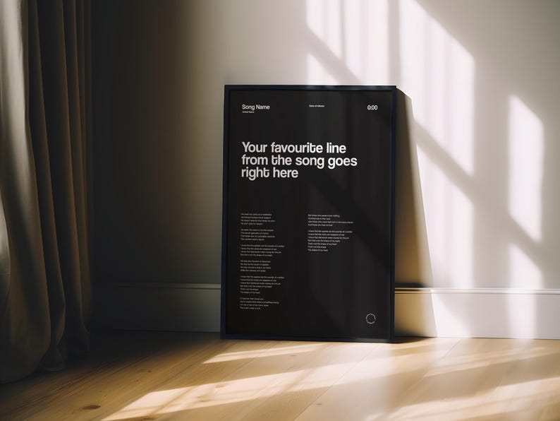 May include: Black framed poster with white text that reads "Your favourite line from the song goes right here." The poster also includes the song name, artist, and a section for the song lyrics. The poster is leaning against a white wall.