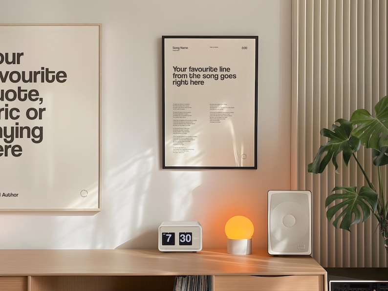 May include: A modern interior scene featuring framed art prints with text, a white digital clock displaying 7:30, a small round lamp, and a white speaker. The artwork includes song lyrics and quotes.
