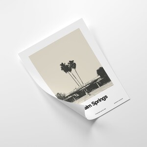 May include: A black and white photograph of Palm Springs City Hall with palm trees in the foreground. The text "Palm Springs" is printed in black at the bottom of the image.