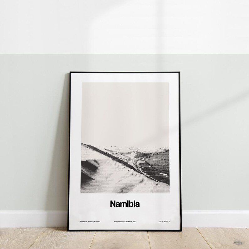 Op de afbeelding: Zwart-witfoto van een woestijnlandschap in Namibi&euml;. De afbeelding toont een grote zandduin met een kustlijn in de verte. De tekst "Namibi&euml;" is onder de afbeelding gedrukt.