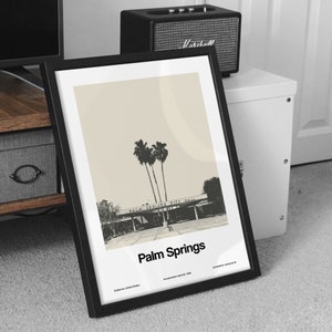 May include: A black framed print with a beige background featuring a black and white photograph of palm trees and a building with the text "Palm Springs City Hall". The print has the text "Palm Springs" in black at the bottom and the text "California, United States Incorporated April 26, 1984" in smaller black text below.