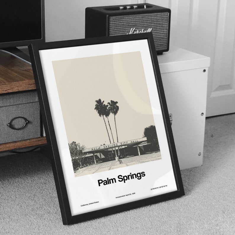 May include: A black framed print with a beige background featuring a black and white photograph of palm trees and a building with the text "Palm Springs City Hall". The print has the text "Palm Springs" in black at the bottom and the text "California, United States Incorporated April 26, 1984" in smaller black text below.