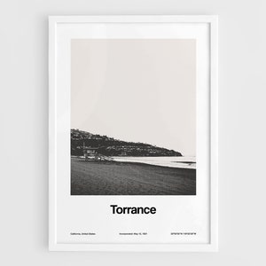 Pode incluir: Fotografia a preto e branco de uma cena de praia com uma cabine de salva-vidas &agrave; dist&acirc;ncia. O texto "Torrance" &eacute; impresso abaixo da imagem, juntamente com a localiza&ccedil;&atilde;o da cidade, a data de incorpora&ccedil;&atilde;o e as coordenadas.