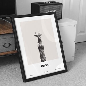 May include: Black and white photo print of the Victory Column in Berlin, Germany. The print is framed in a black frame and has the text "Berlin" and "Founded 1237" printed below the image.