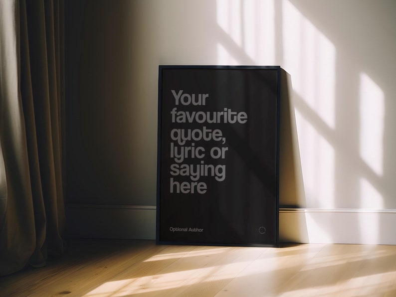May include: A black framed poster with the text "Your favourite quote, lyric or saying here" in a white sans-serif font. The poster is leaning against a white wall and a wooden floor. The words "Optional Author" are at the bottom.