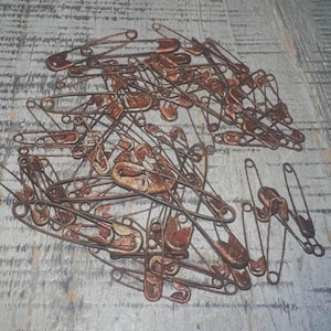 May include: A large pile of rusty safety pins. The pins are all different sizes and shapes, and some are bent or broken.