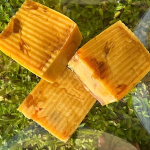 May include: Three bars of handmade soap with a yellow and orange swirl pattern. The soap is made with natural ingredients and is perfect for sensitive skin.