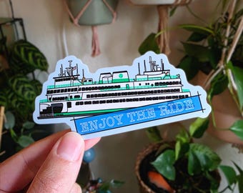 May include: A sticker featuring a ferry boat design with green and white accents. The sticker has the words "Enjoy the Ride" in a blue banner across the bottom. The ferry has multiple decks and windows.