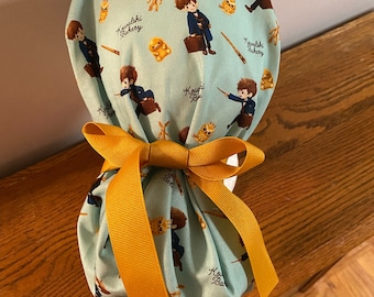 Könnte beinhalten: Eine blaue Stofftasche mit gelbem Band. Die Tasche ist mit einem sich wiederholenden Muster eines Jungen mit Zauberstab und Koffer verziert, auf der Tasche steht "Kawalski Bakery".