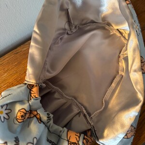 May include: A light blue satin scrub hat with a print of golden retrievers and the text "Life is golden" and "Life is unique". The hat has a gray satin lining.