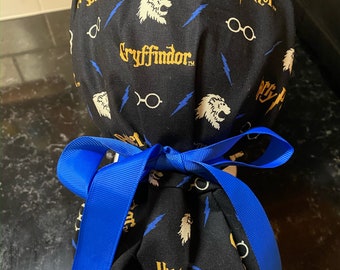 Könnte beinhalten: Schwarze OP-Mütze mit einer blauen Schleife. Die Mütze hat ein sich wiederholendes Muster aus Harry-Potter-Motiven, darunter der Gryffindor-Löwe, Blitze und Harry Potters Brille.