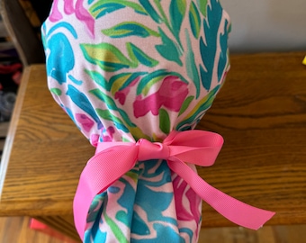 Puede incluir: Un gorro quirúrgico de color rosa y azul con estampado floral y una cinta de satén rosa atada en un lazo.